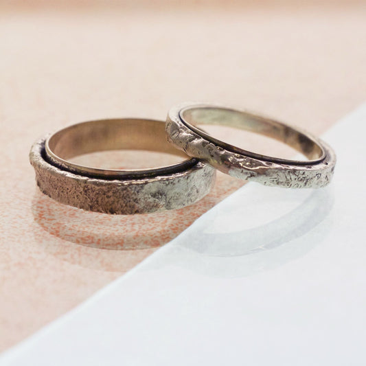 Two matching wedding bands, the slimmer band rests on top of a thicker band. Both a beautiful and unusual with a polished thin inner band and a rough, raw textured outer band. Made in oxidised recycled sterling silver.
