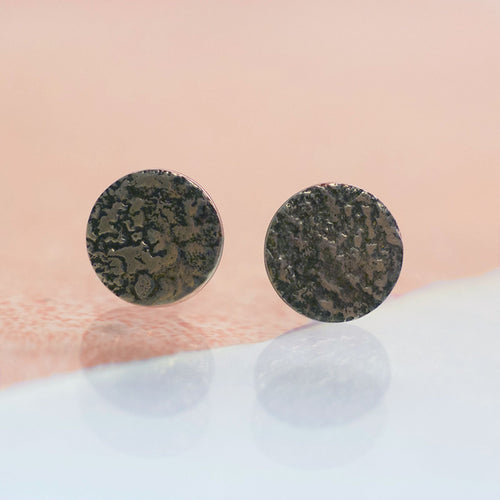 A pair of full moon stud earrings with ear sticks. Rough raw organic texture on flat round earrings. The silver is oxidised so the texture is accentuated in with black on the silver. handmade with a moonscape texture to resemble the surface of the moon. Made in Copenhagen by Scottish designer Caroline Cloughley. 